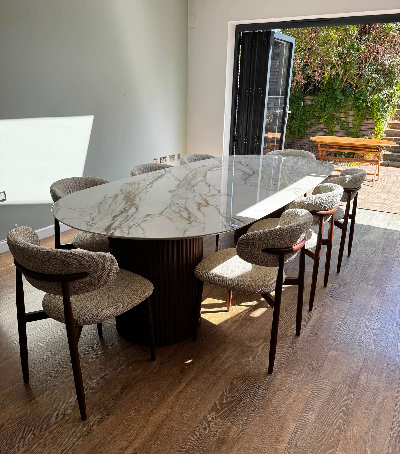 Veined stone dining table with upholstered chairs beside open garden doors