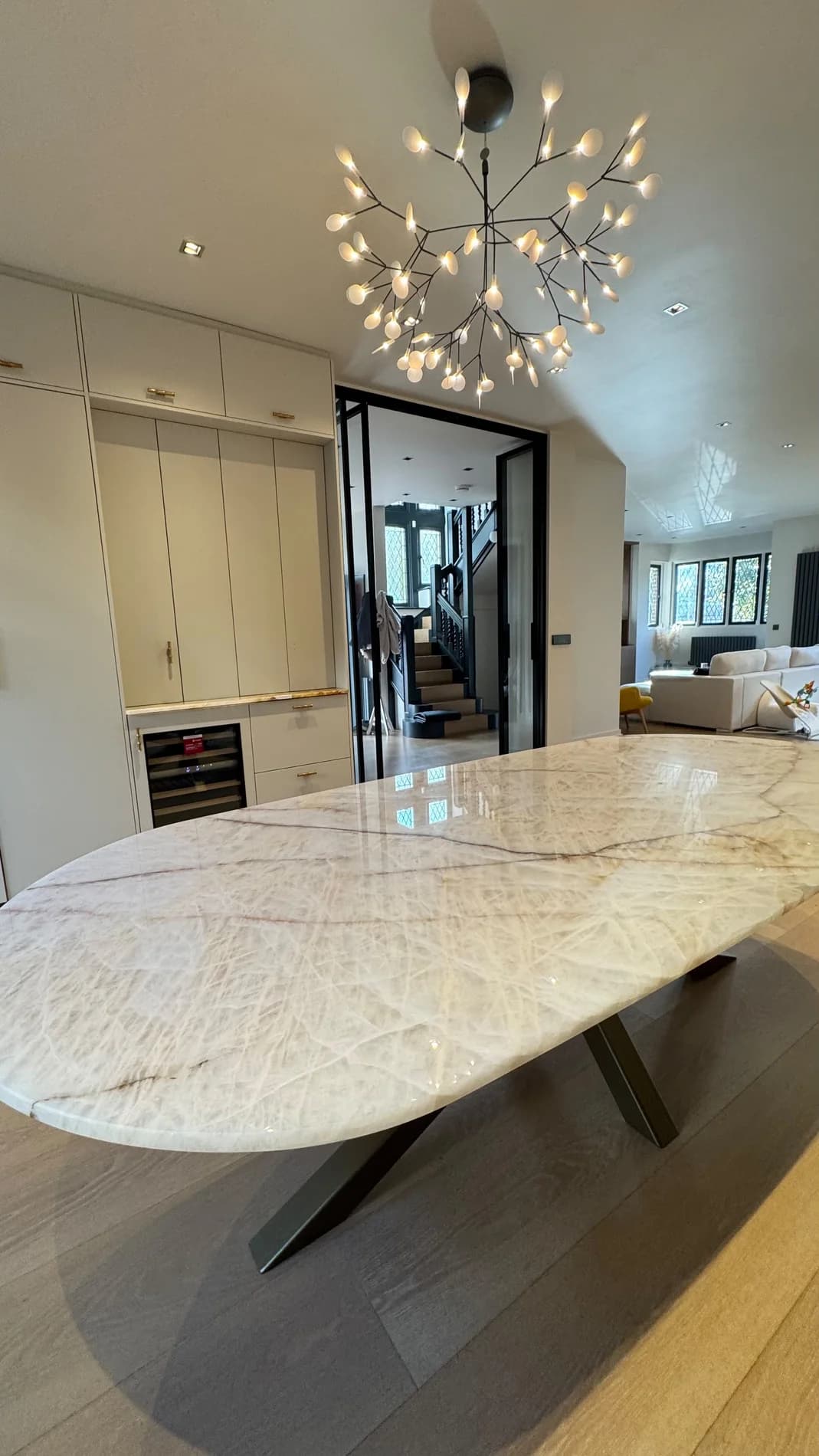 Oval veined stone dining table with a dark sculptural base beneath pendant lighting